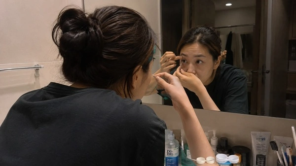 Contact lens wearer removing lenses at the end of the day while evaluating comfort and eye dryness.